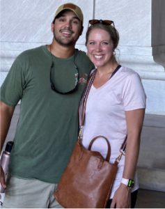 Two people are smiling inside a building with stone walls. The setting appears to be the Lincoln Memorial in Washington, D.C.